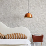 A modernist bed, hanging lamp and chair stand in front of a wall papered in an abstract linear print in white and cream.