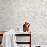 A bench with a towel and clay vases stands in front of a wall papered in an abstract linear print in cream and white.