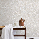 A bench with a towel and clay vases stands in front of a wall papered in an abstract linear print in cream and white.