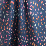 Draped fabric yardage in a playful paint blotch print in shades of pink, blue and orange on a navy field.