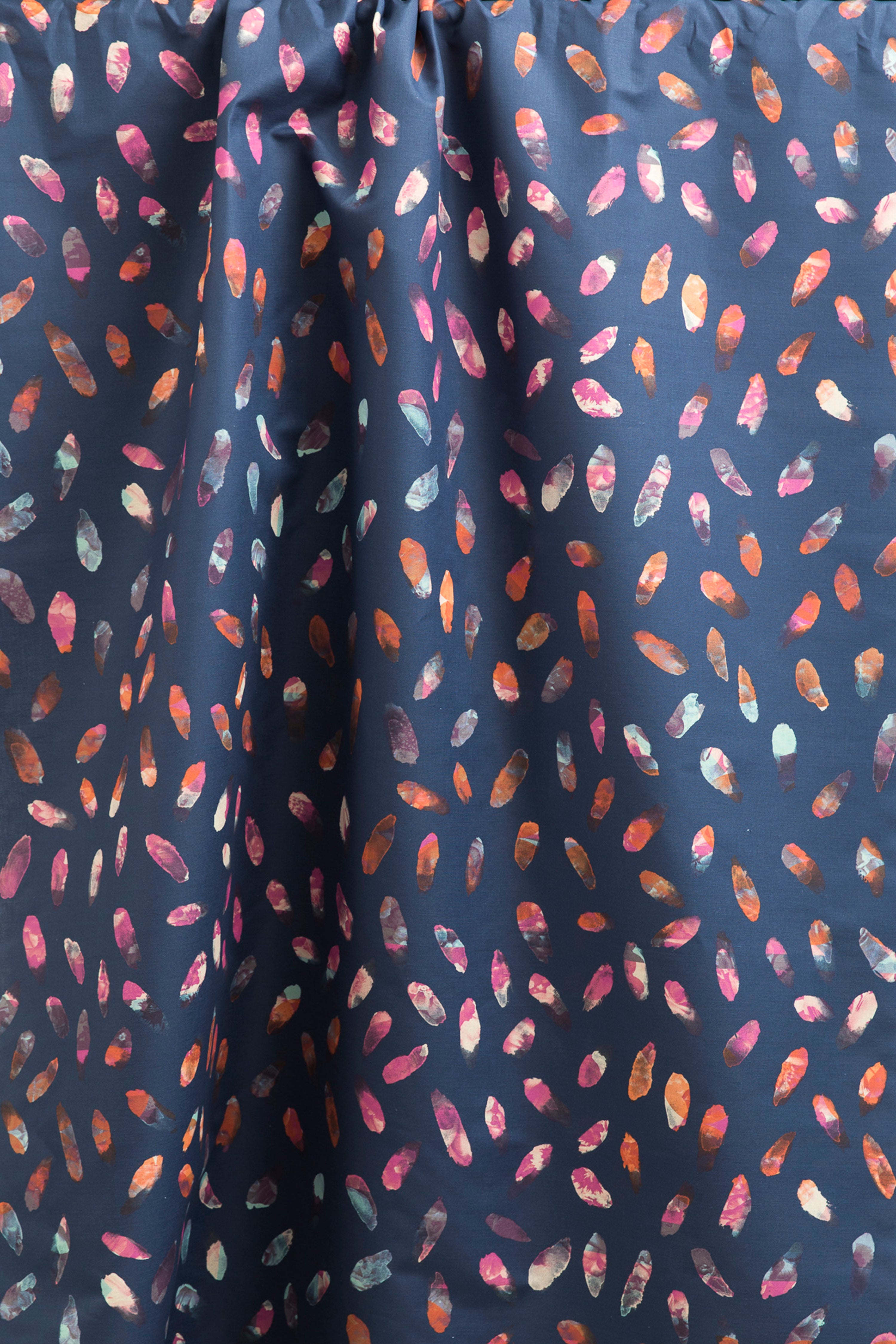 Draped fabric yardage in a playful paint blotch print in shades of pink, blue and orange on a navy field.