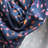 Crumpled fabric yardage in a playful paint blotch print in shades of pink, blue and orange on a navy field.