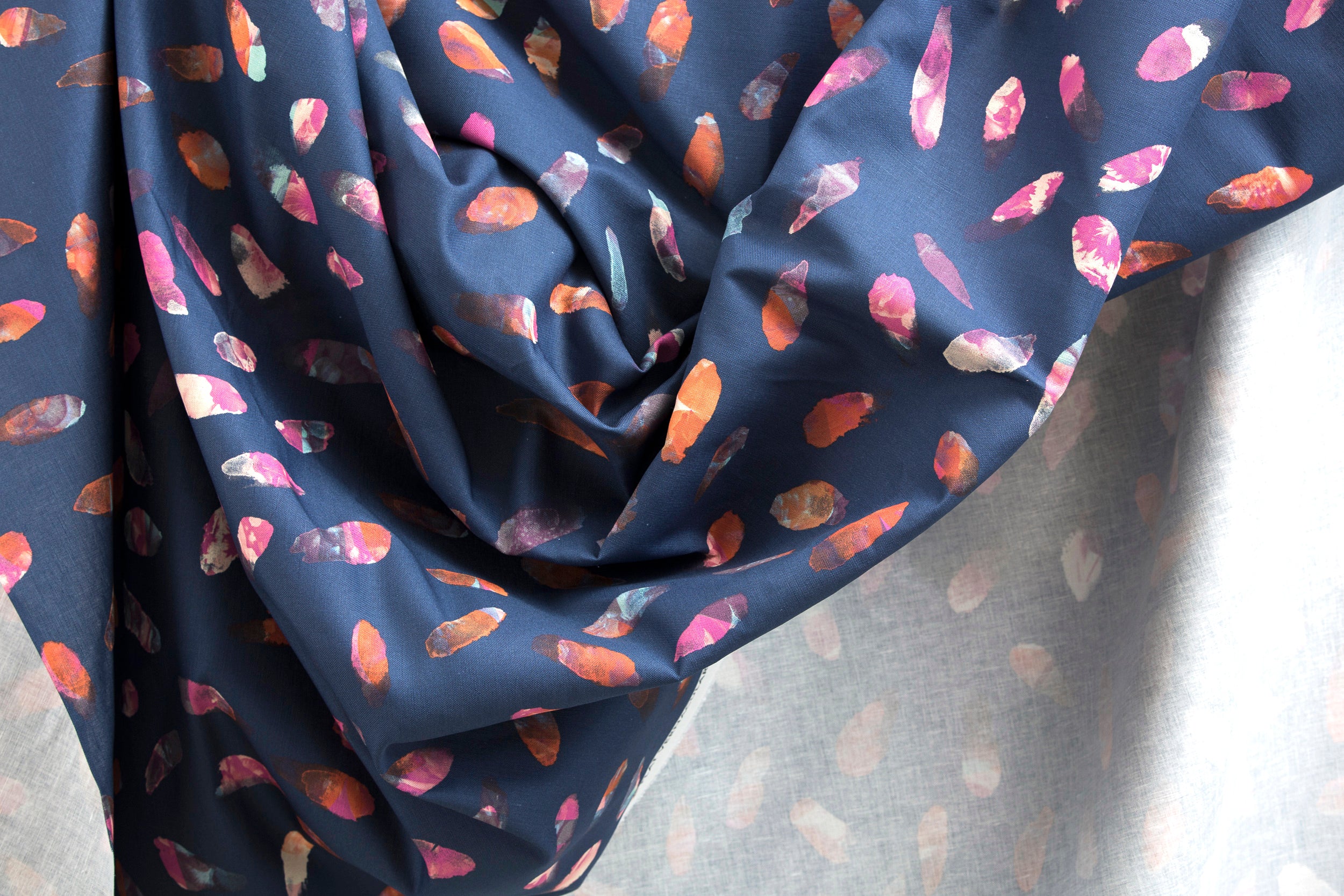 Crumpled fabric yardage in a playful paint blotch print in shades of pink, blue and orange on a navy field.