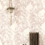 A living space with a radiator, a plant and a wall papered in an abstract floral print in mottled pink, gray and white.