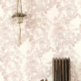 A living space with a radiator, a plant and a wall papered in an abstract floral print in mottled pink, gray and white.