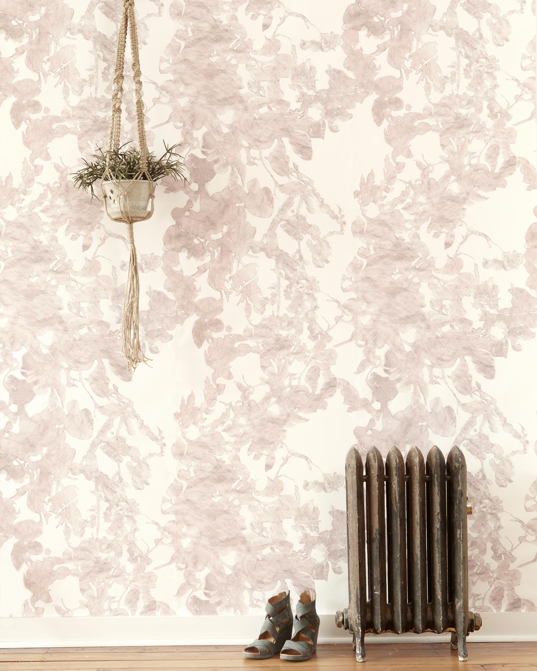 A living space with a radiator, a plant and a wall papered in an abstract floral print in mottled pink, gray and white.