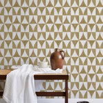 A bench with a towel and clay vases stands in front of a wall papered in a curvilinear grid print in mustard and white.