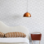 A modernist bed, hanging lamp and chair stand in front of a wall papered in a curvilinear grid print in white and light gray.