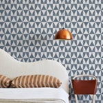 A modernist bed, hanging lamp and chair stand in front of a wall papered in a curvilinear grid print in navy and white.