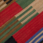 Detail of a handwoven runner in a stacked stripe pattern in blue, red, green , tan and black.