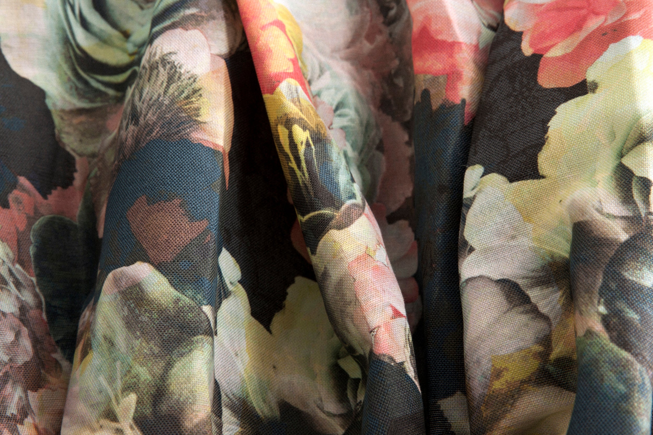 Close-up of draped fabric in a dense photorealistic floral print in shades of pink, green and black.