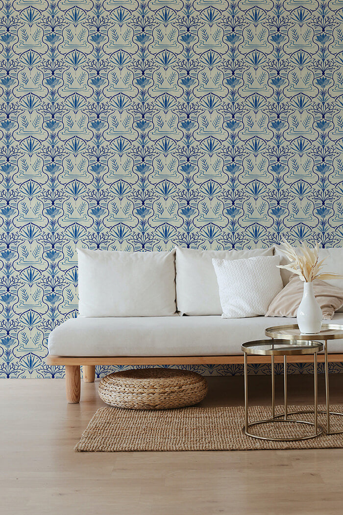 A couch and wooden end table stand in front of a wall papered in an intricate floral lattice print in blue and cream.