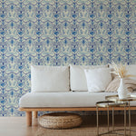 A couch and wooden end table stand in front of a wall papered in an intricate floral lattice print in blue and cream.