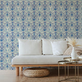 A couch and wooden end table stand in front of a wall papered in an intricate floral lattice print in blue and cream.