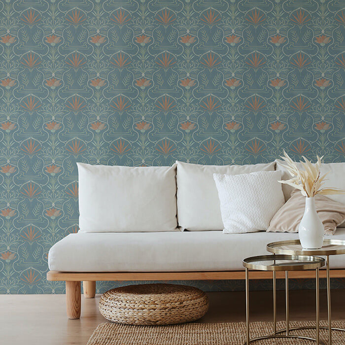 A couch and wooden end table stand in front of a wall papered in an intricate floral lattice print in green, coral and blue.