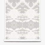 Partially unrolled wallpaper yardage in a painterly ikat print in shades of gray and cream.