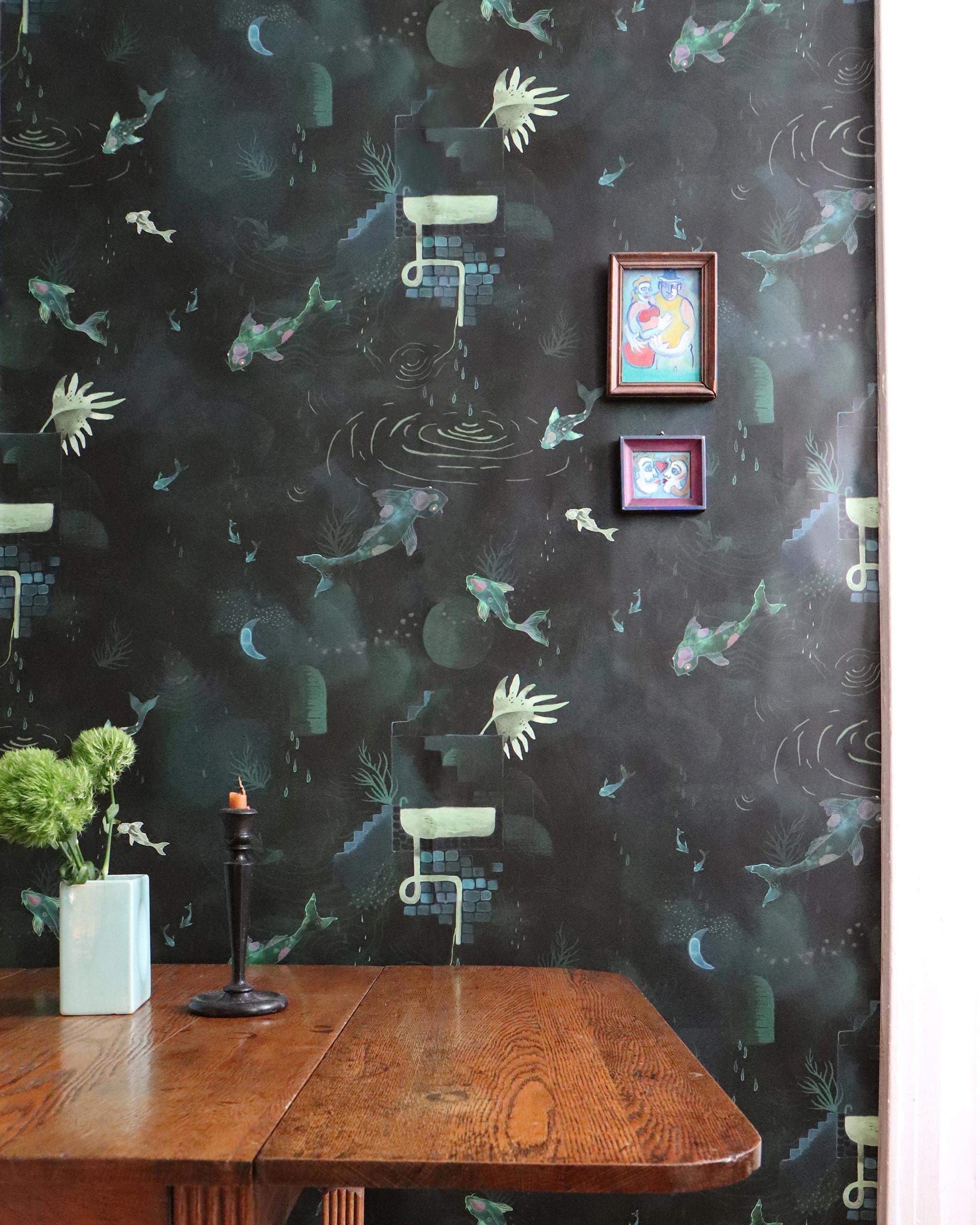 A dining room table stands in front of a wall papered in a playful koi pond print in green, yellow and black.