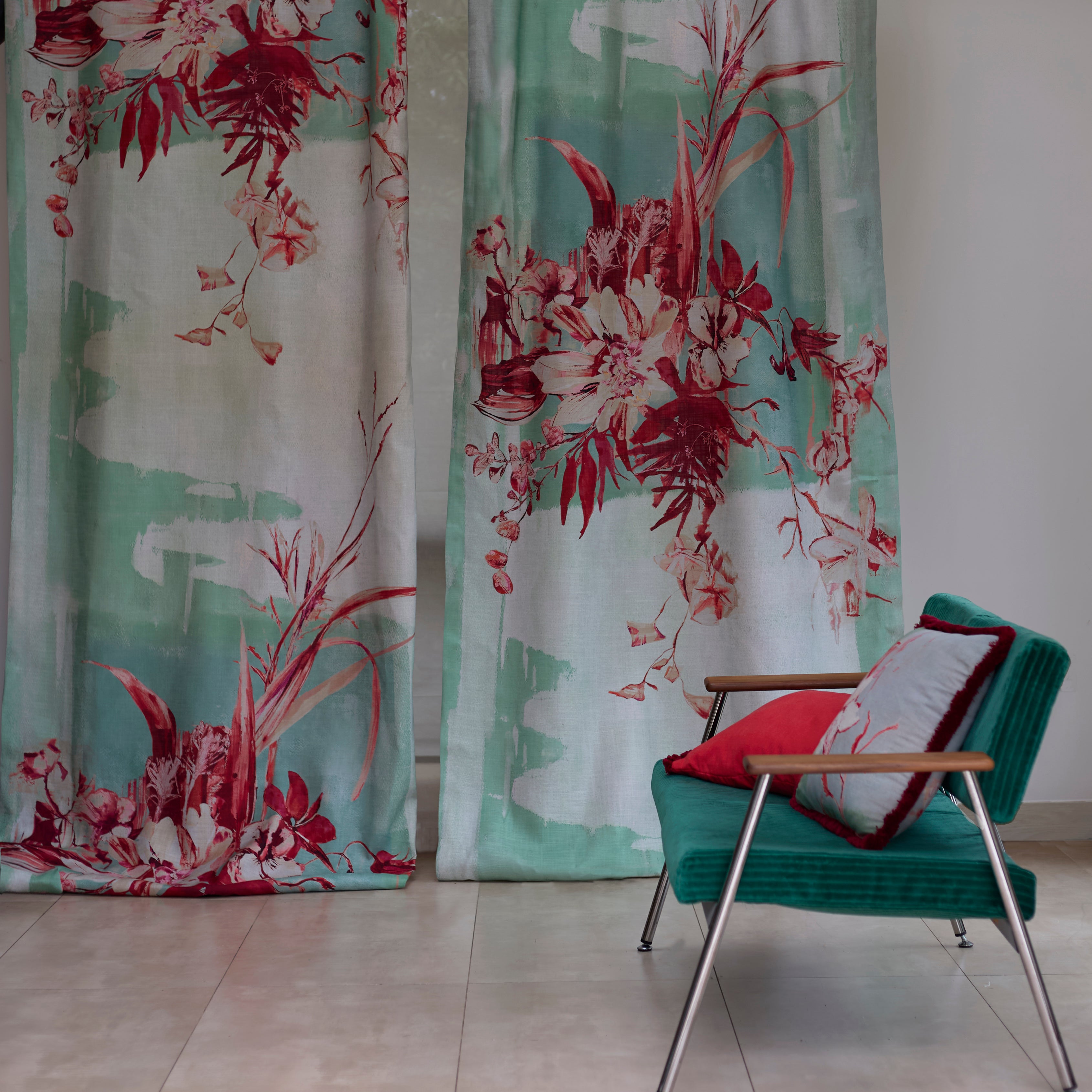 Two curtain panels in a watercolor mural in red and tuquoise with a side chair and throw pillows