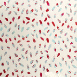 A vase of flowers stands in front of a wall covered in a playful paint blotch print in red and blue on a cream field.