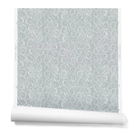 A hanging roll of wallpaper with a large-scale repeating leaf print in white on a blue-gray watercolor background.