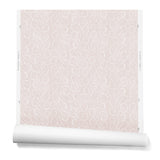 A hanging roll of wallpaper with a large-scale repeating leaf print in white on a light pink watercolor background.