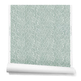 A hanging roll of wallpaper with a large-scale repeating leaf print in white on a sage green watercolor background.