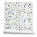 A hanging roll of wallpaper in a large-scale minimal floral print in shades of navy, blue-gray and green on a white background.