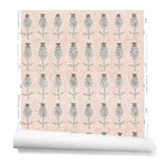 A hanging roll of wallpaper with repeating rows of a watercolor flowers in tan and gray on a light pink background.