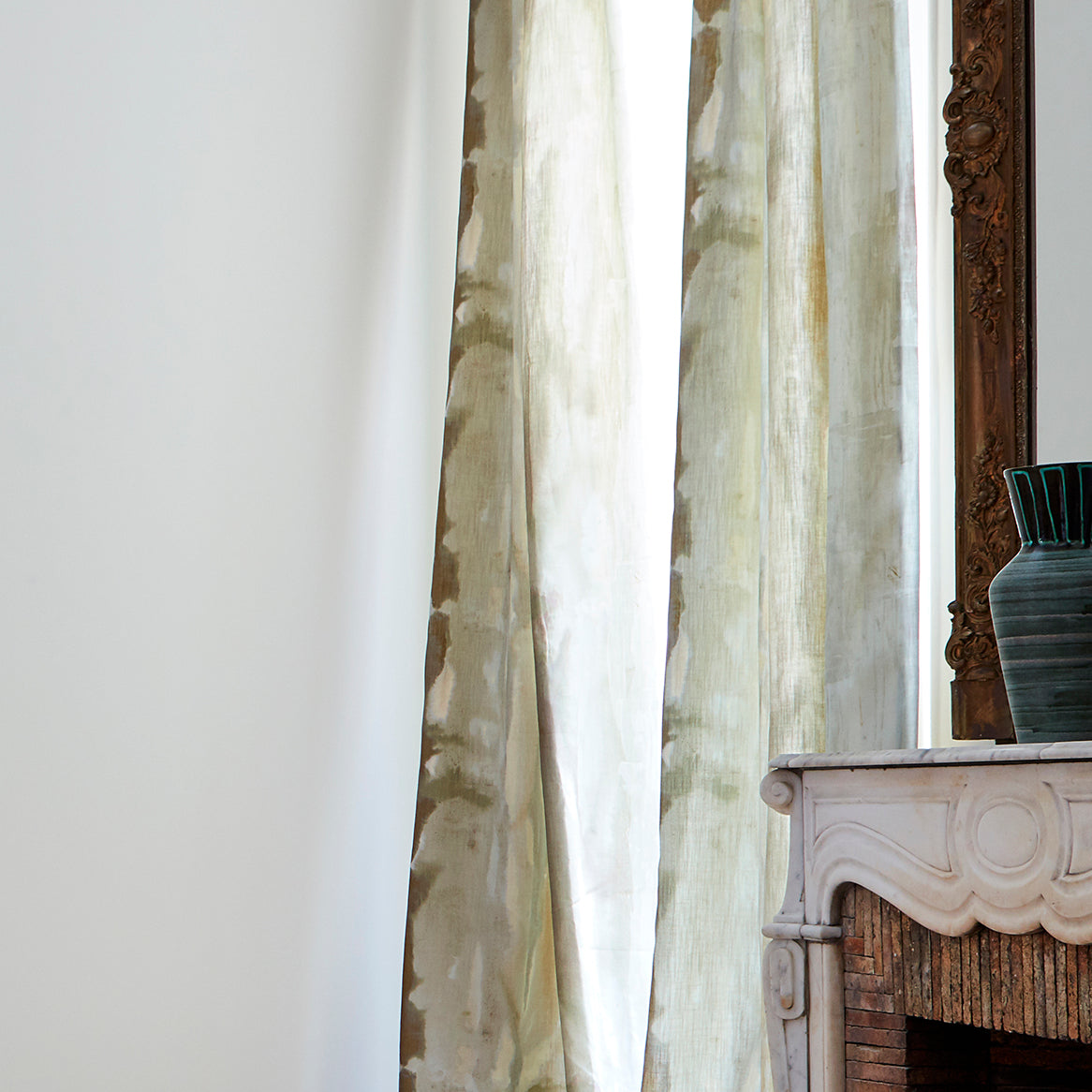 A sunny living space with long curtains in an abstract paint swatch print in shades of brown, gray and blue.