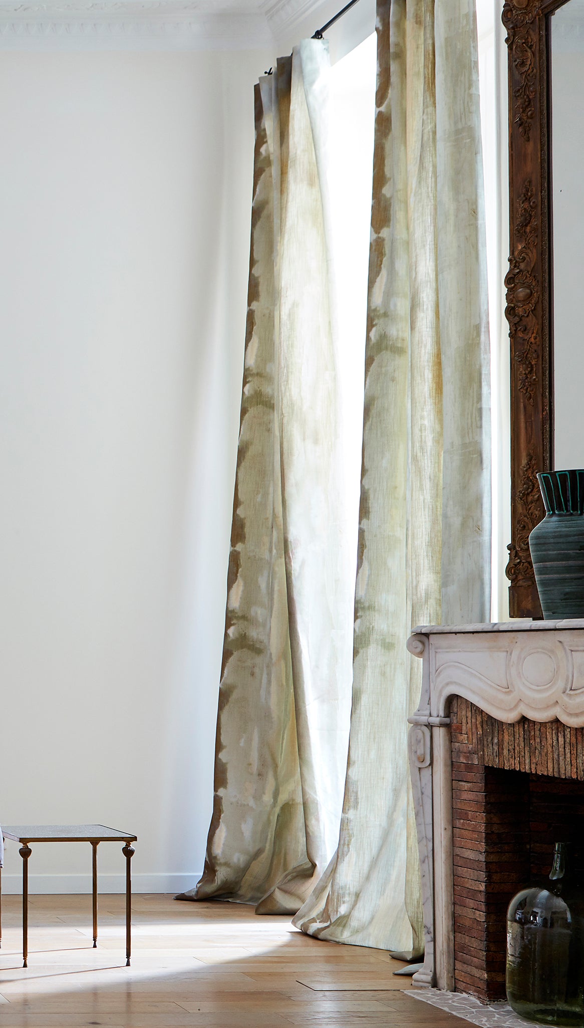 A sunny living space with long curtains in an abstract paint swatch print in shades of brown, gray and blue.