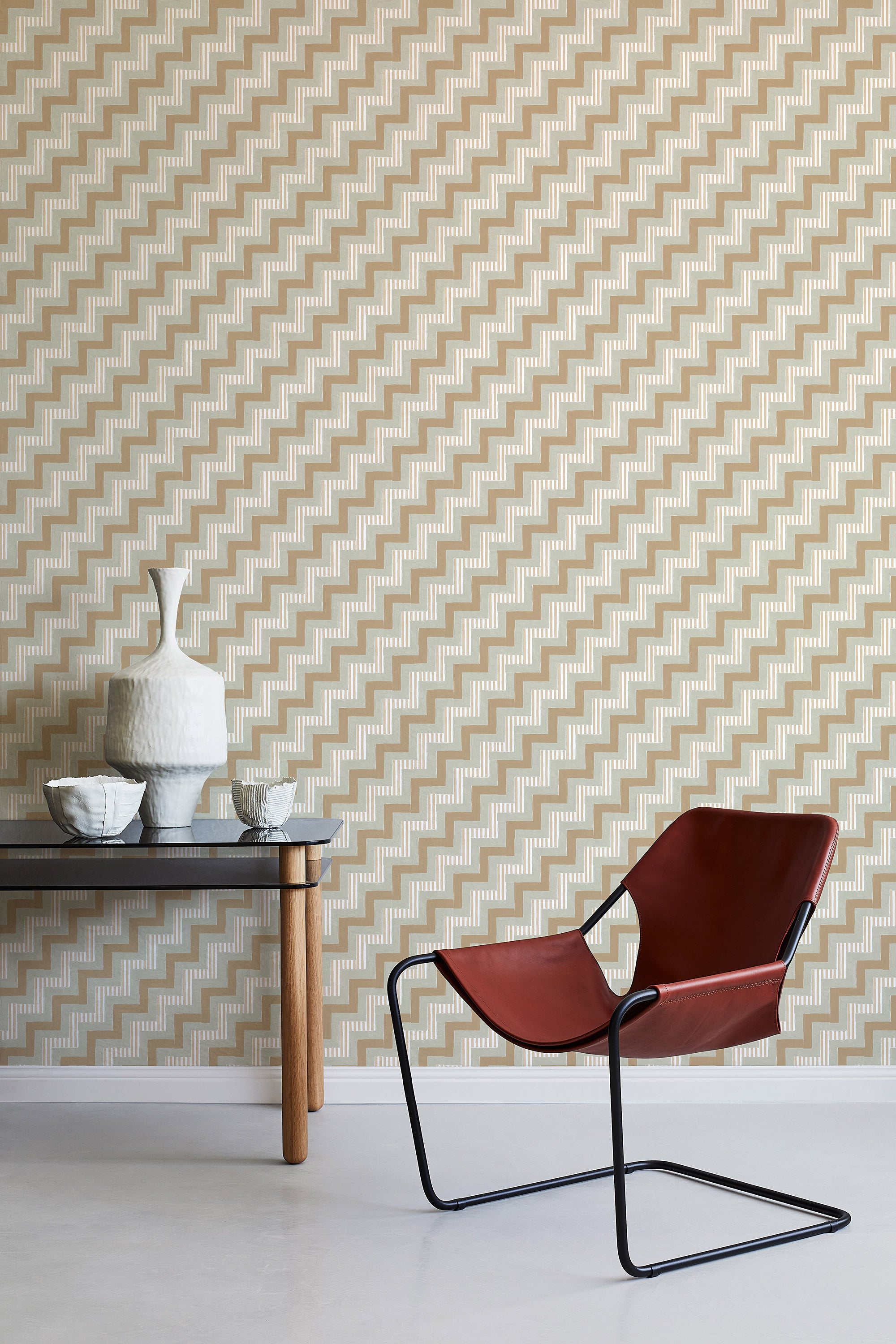 A modernist armchair stands in front of a wall papered in a playful zigzag stripe print in shades of brown, gray and white.