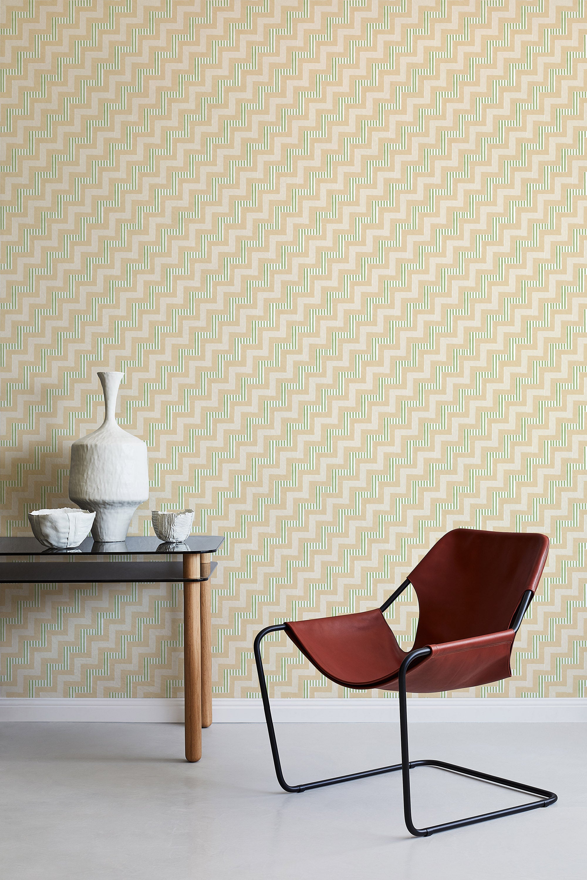 A modernist armchair stands in front of a wall papered in a playful zigzag stripe print in shades of pink, beige and green.