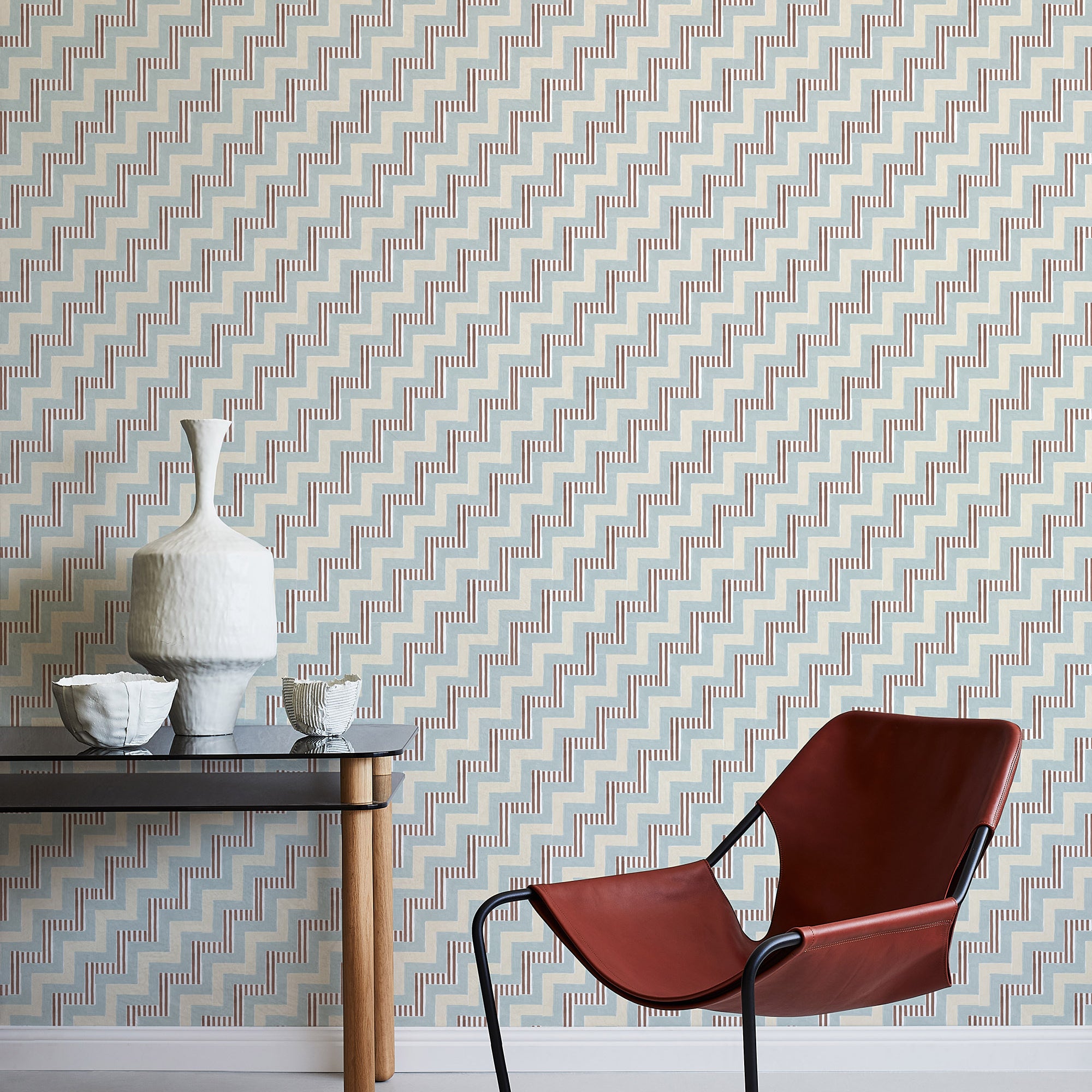 A modernist armchair stands in front of a wall papered in a playful zigzag stripe print in shades of beige, blue and brown.