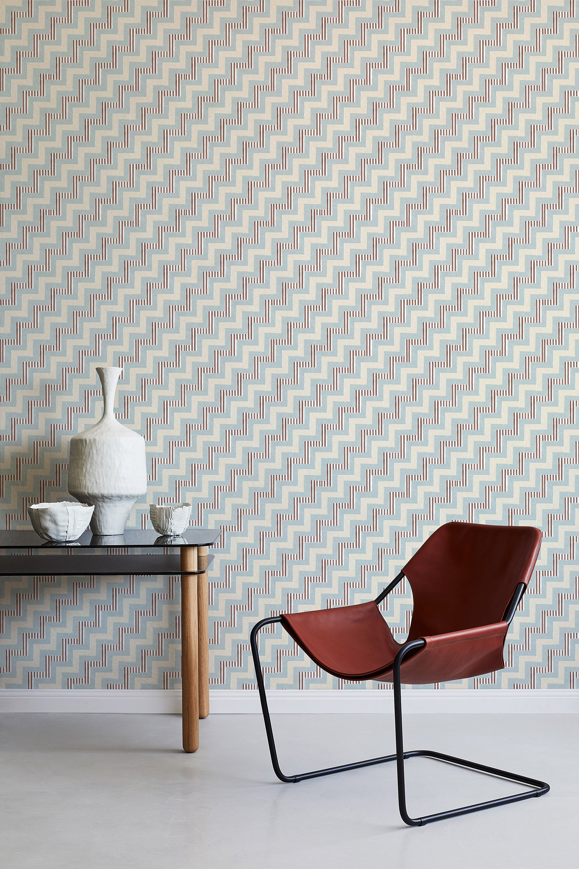 A modernist armchair stands in front of a wall papered in a playful zigzag stripe print in shades of beige, blue and brown.