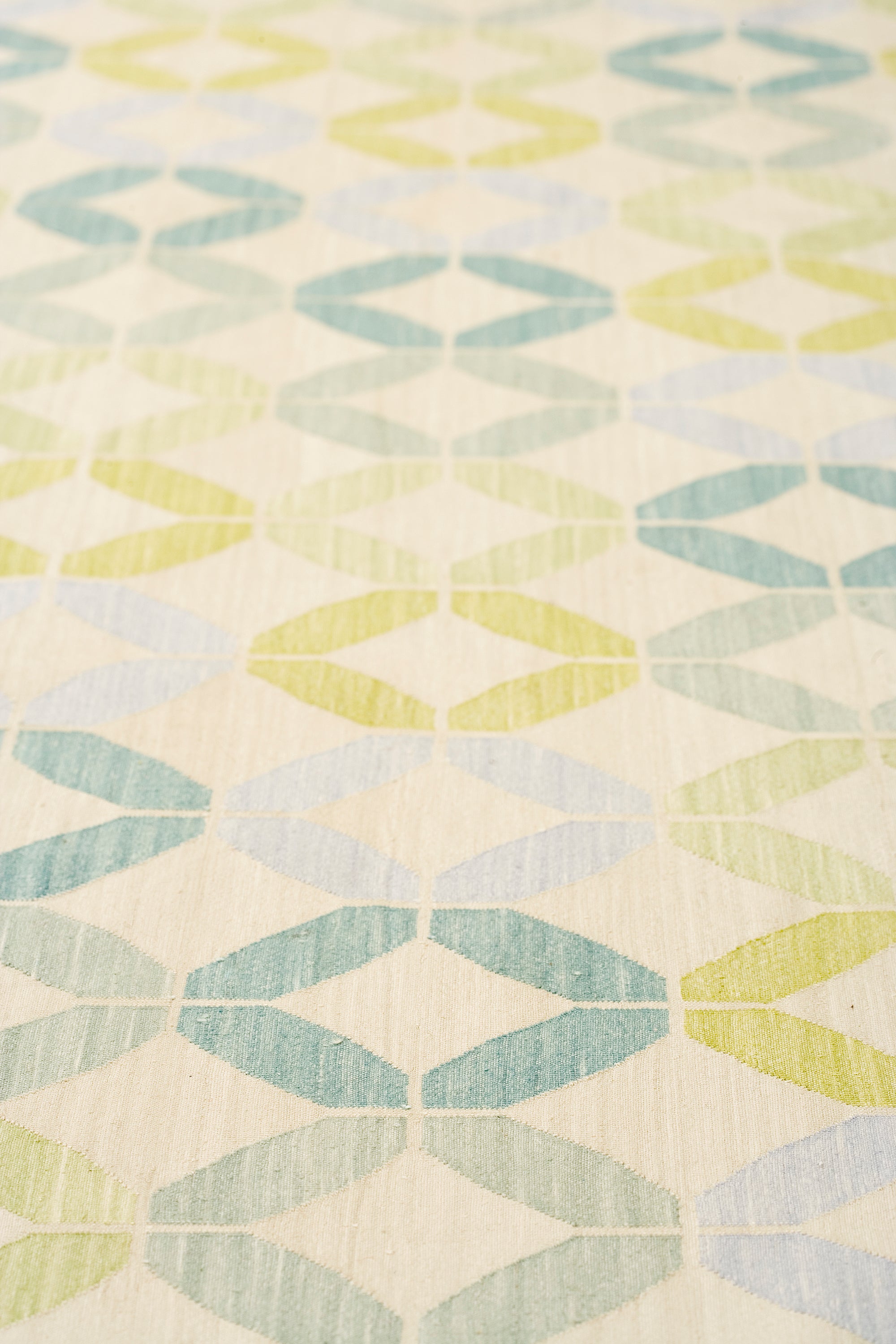 Detail of Alhambra Rug in Mint featuring a pattern of linked circles that create a star like lattice in a range of pastel turquoise, mint, yellow and lime green on a soft beige field. 
