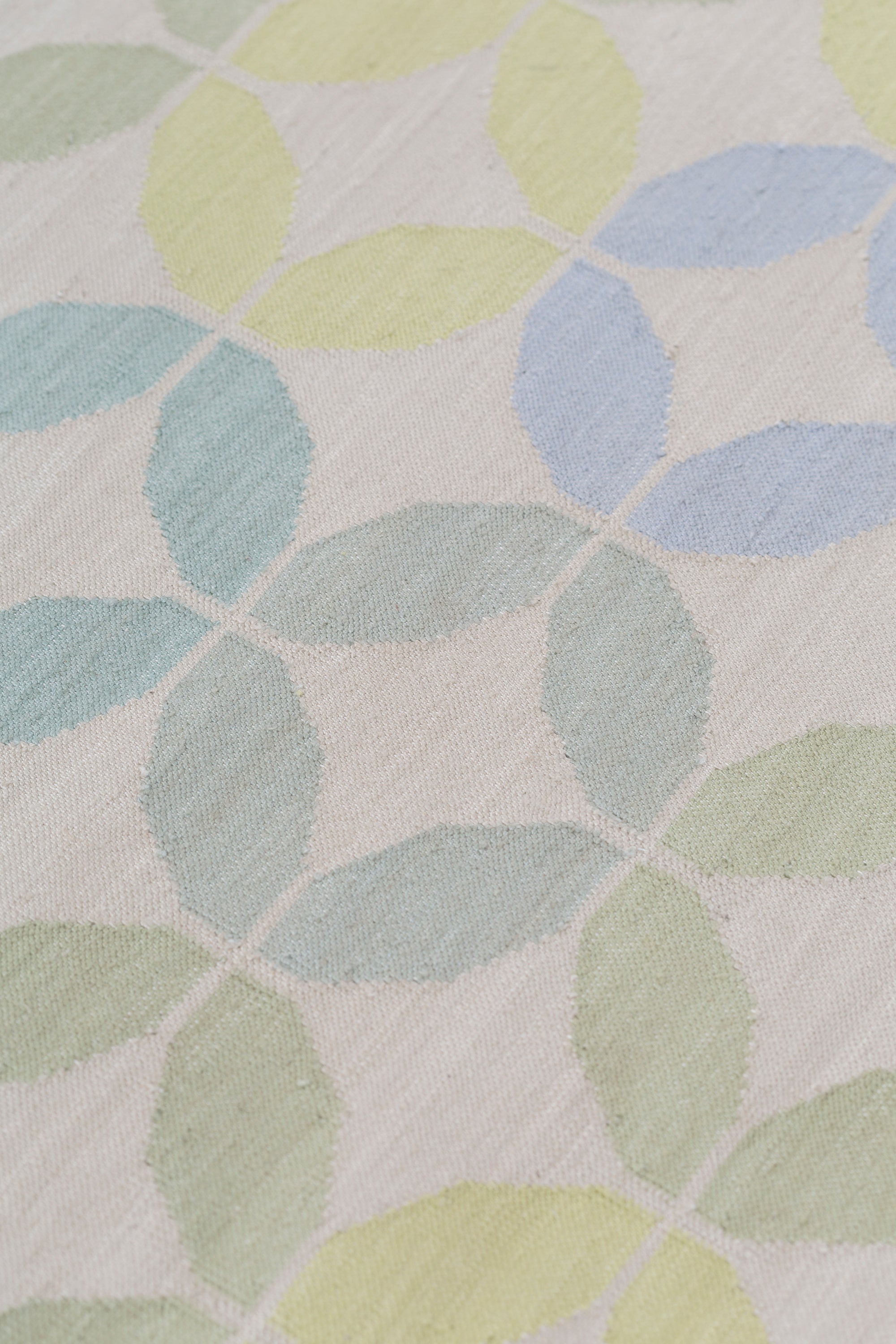 Detail of Alhambra Rug in Mint featuring a pattern of linked circles that create a star like lattice in a range of pastel turquoise, mint, yellow and lime green on a soft beige field. 