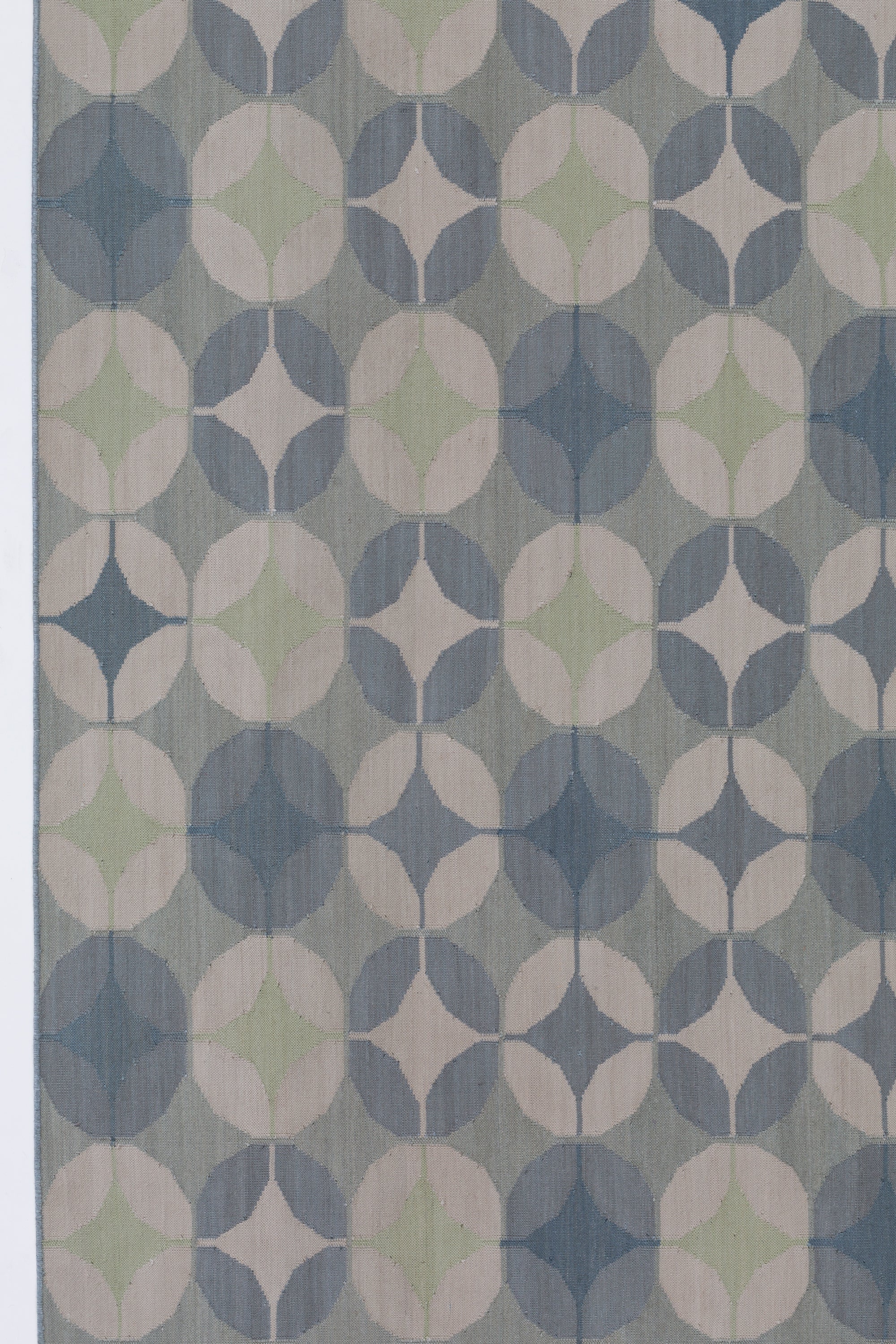 Detail of Alhambra Rug in Seafret featuring pattern of linked circles that create a star like lattice in a range of pale blues, with a light green accent on a soft white field. 