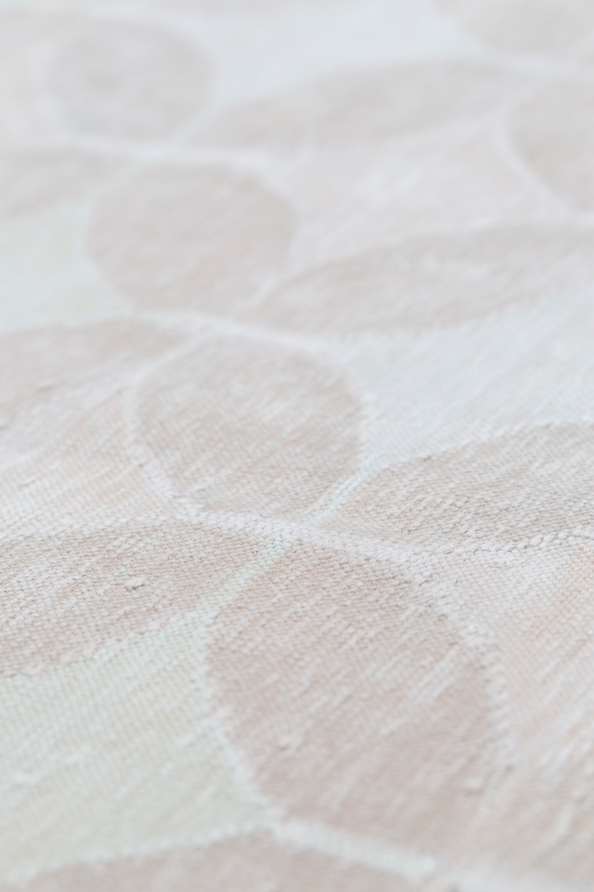 Detail of Alhambra Rug in Stonewash featuring pattern of linked circles that create a star like lattice in a range of pale pink tones a soft white field. 