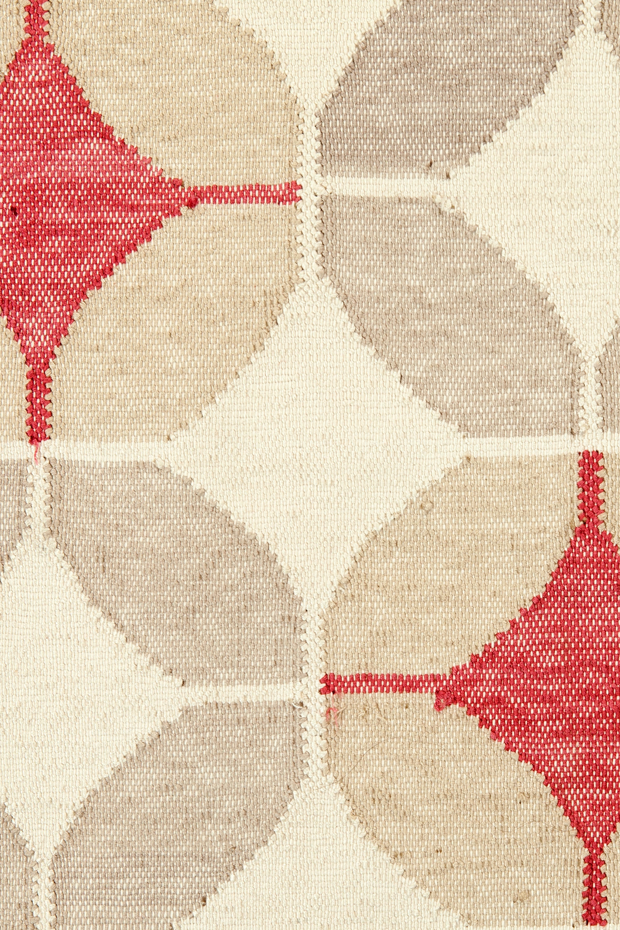 Detail of Alhambra Rug in Tomato featuring pattern of linked circles that create a star like lattice in a range of tan, beige, ecru and bright red on a soft white field. 
