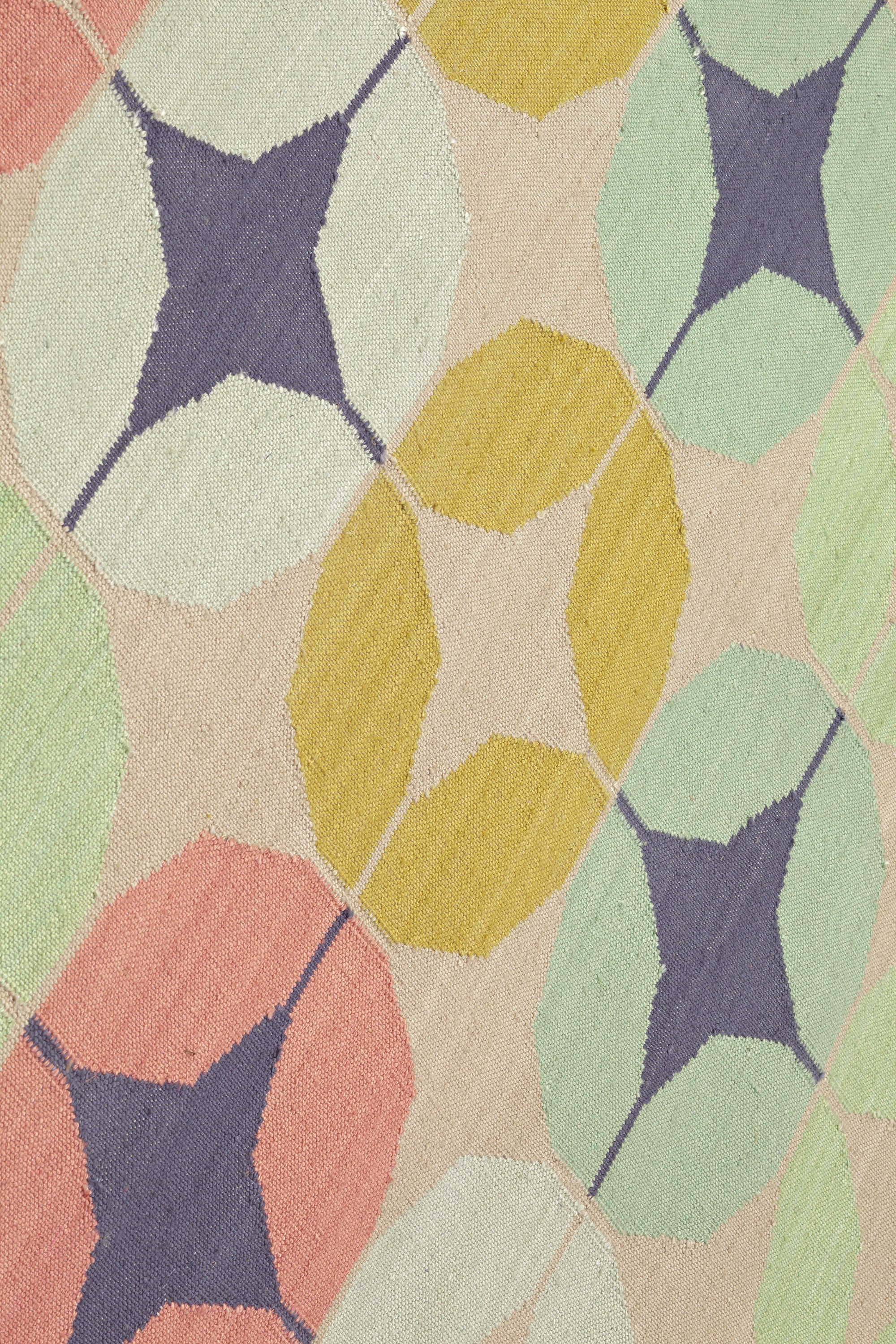 Detail of Alhambra Rug in Venetia featuring pattern of linked circles that create a star like lattice in a range of coral, mustard tyellow, seafoam green, pale green and royal purple accents on a tan field. 