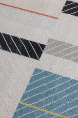 Detail of the Amelia Rug in Camara featuring a minimalist broken stripe pattern, overlayed with thin white diagonal lines. The broken stripes are a mix of black, pale blue and turquoise with accents of red and bright yellow, all on a soft grey field