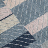 Detail of the Amelia Rug in Lapiz featuring a minimalist broken stripe pattern, overlayed with thin light blue diagonal lines. The broken stripes are a mix of navy blue, pale blue. white and turquoise with black accents, all on denim blue field.