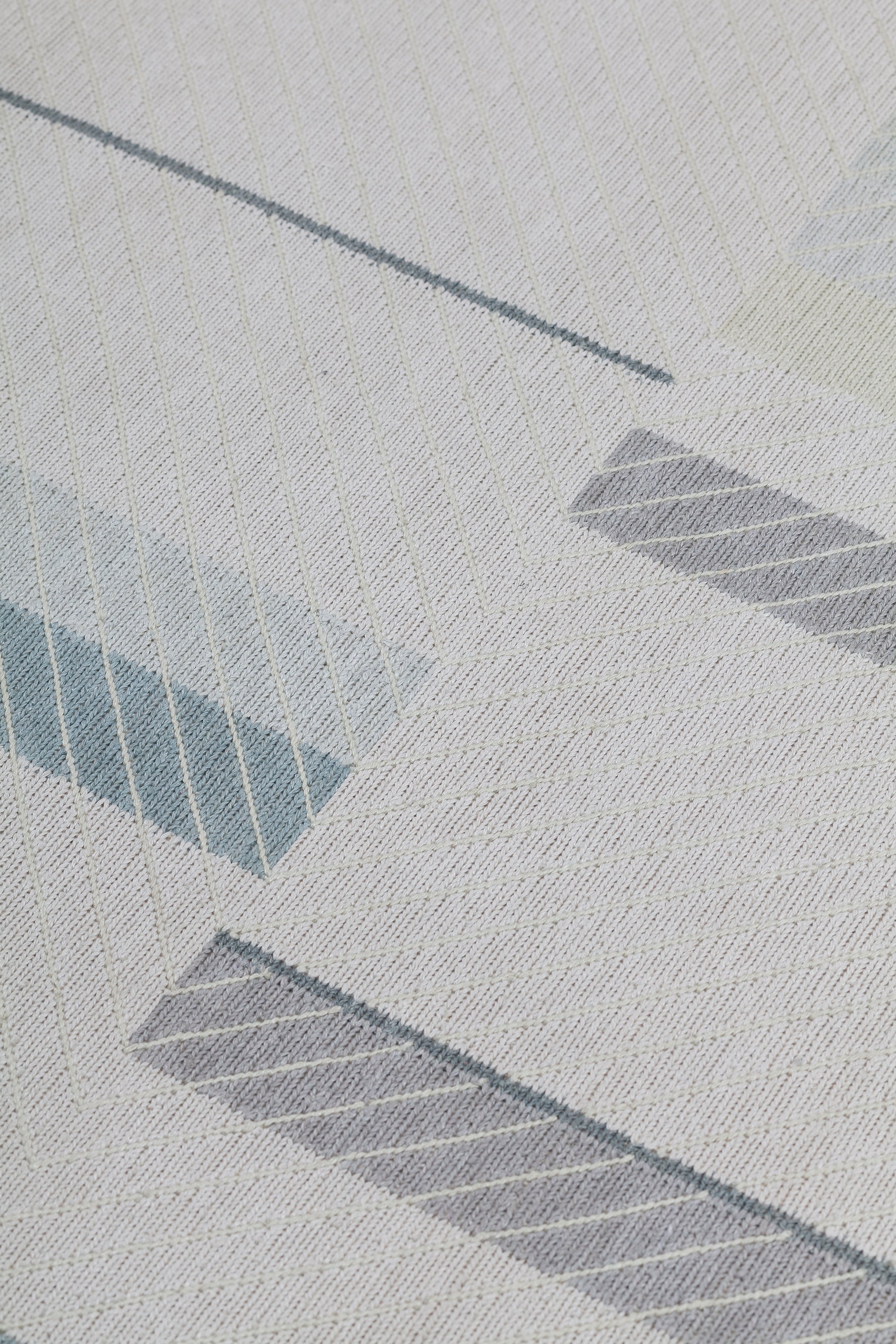 Detail of the Amelia Rug in Pearl featuring a minimalist broken stripe pattern, overlayed with thin white diagonal lines. The broken stripes are a mix of pale blues, grey, and turquoise with slate grey accents, all on a pale grey field. 