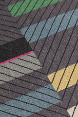 Detail of the Amelia Rug in Spinel featuring a minimalist broken stripe pattern, overlayed with thin black diagonal lines. The broken stripes are a mix of white, grey, kelly green, denim blue, black with hot pink accents, all on a charcoal grey field. 