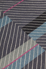 Detail of the Amelia Rug in Spinel featuring a minimalist broken stripe pattern, overlayed with thin black diagonal lines. The broken stripes are a mix of white, grey, kelly green, denim blue, black with hot pink accents, all on a charcoal grey field. 