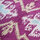Detail of the Anna Ikat rug in Cranberry features an ikat inspired pattern of diamonds in blue and white with pale lime green accents on a magenta field