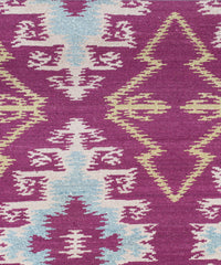 Detail of the Anna Ikat rug in Cranberry features an ikat inspired pattern of diamonds in blue and white with pale lime green accents on a magenta field