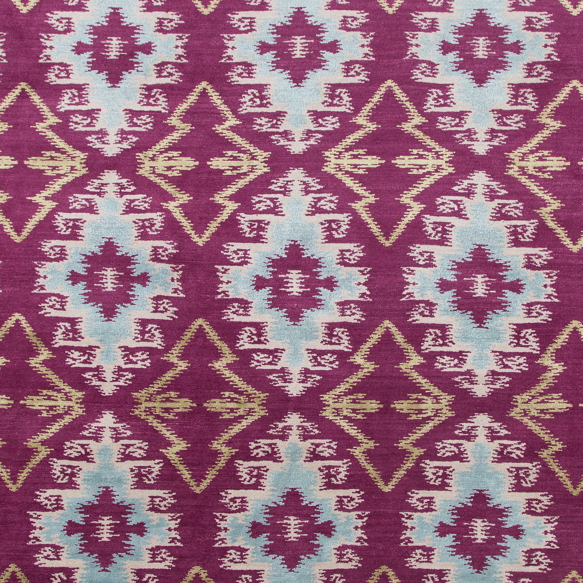 Full Size Anna Ikat rug in Cranberry features an ikat inspired pattern of diamonds in blue and white with pale lime green accents on a magenta field