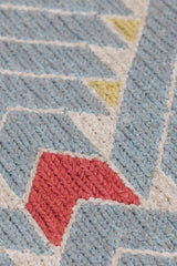 Detail of the Arrow Rug in Powder Blue-Coral features a dense pattern of nesting arrow shapes in soft blue with accents of coral and yellow on an ivory field. 