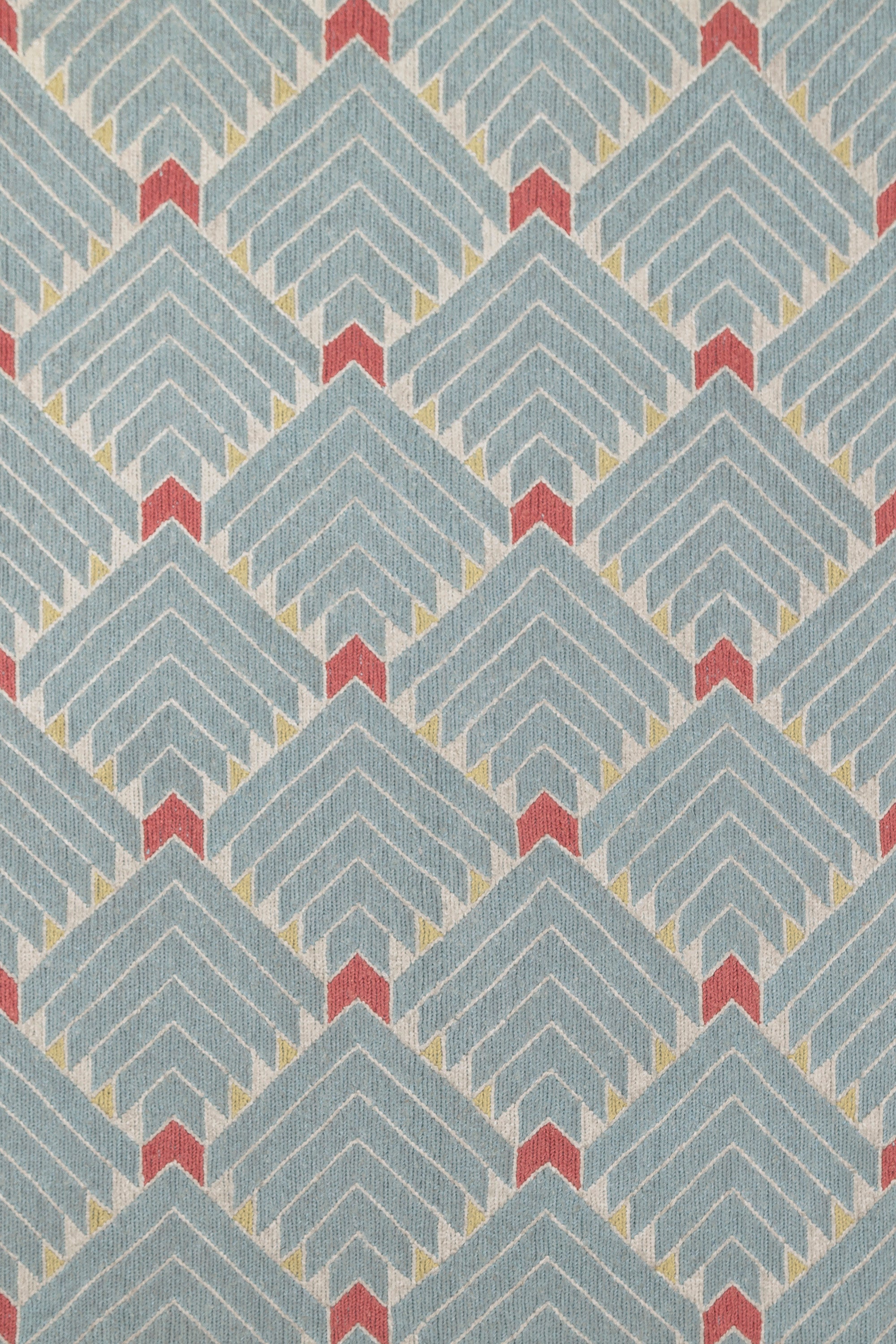 The Arrow Rug in Powder Blue-Coral features a dense pattern of nesting arrow shapes in soft blue with accents of coral and yellow on an ivory field. 